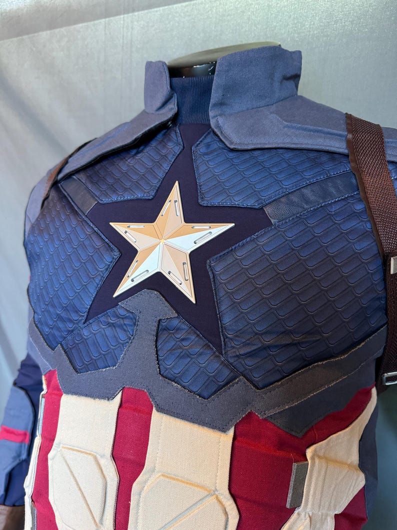Puede incluir: Un traje de superh&eacute;roe azul y rojo con un emblema en forma de estrella en el pecho. El traje tiene una tela texturizada y un dise&ntilde;o acolchado.