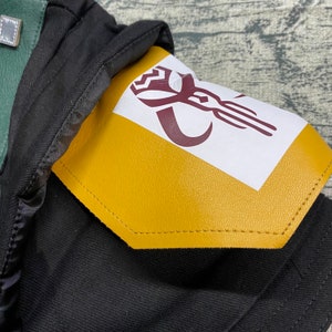 May include: A black jacket with a yellow patch on the shoulder. The patch has a white background with a maroon symbol on it.