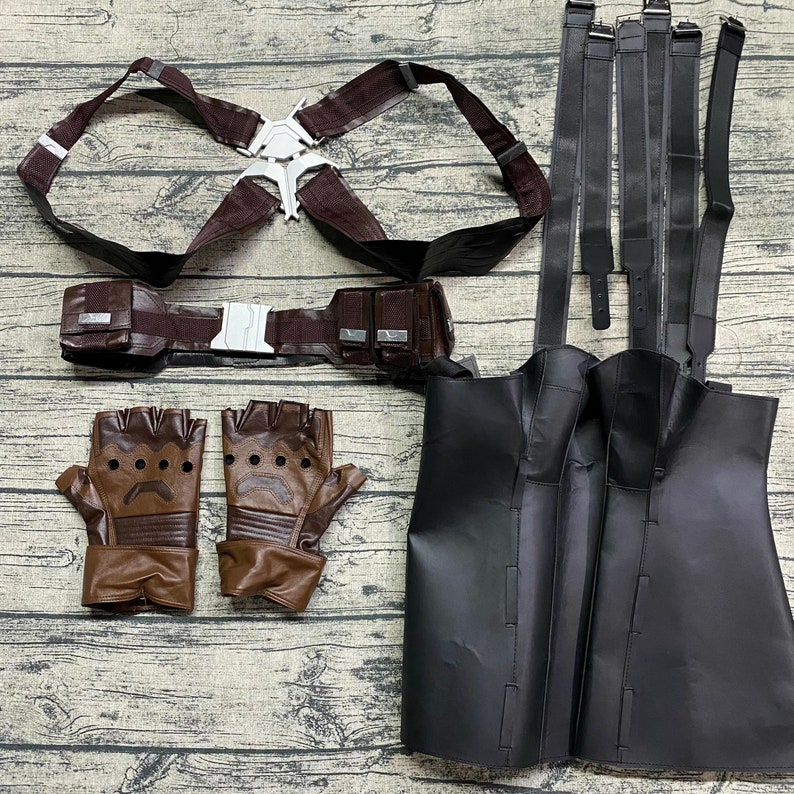 Puede incluir: Un conjunto de disfraz de cuero marr&oacute;n con arn&eacute;s, cintur&oacute;n, guantes y falda de cuero negro. El arn&eacute;s tiene una hebilla plateada y el cintur&oacute;n tiene hebillas plateadas y bolsas. Los guantes son sin dedos y de cuero marr&oacute;n y negro.