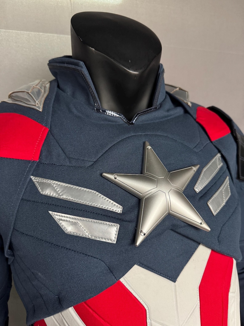 Puede incluir: Un traje de superh&eacute;roe azul y rojo con una estrella plateada en el pecho. El traje tiene un cuello alto y una cremallera en la parte delantera.
