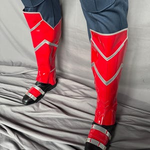 Puede incluir: Botas rojas y plateadas con correas negras. Las botas est&aacute;n hechas de un material brillante y tienen una punta puntiaguda.