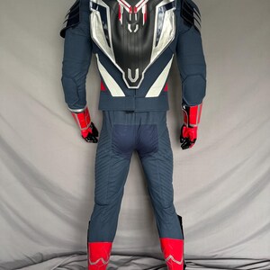 Puede incluir: Un traje de superh&eacute;roe azul y rojo con una placa de pecho plateada y blanca y una placa trasera negra. El traje tiene un dise&ntilde;o rojo y blanco en los brazos y las piernas.