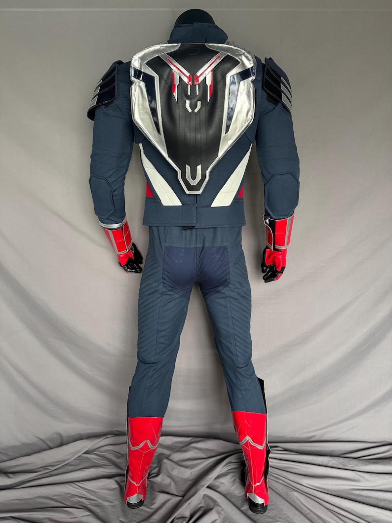 Puede incluir: Un traje de superh&eacute;roe azul y rojo con una placa de pecho plateada y blanca y una placa trasera negra. El traje tiene un dise&ntilde;o rojo y blanco en los brazos y las piernas.