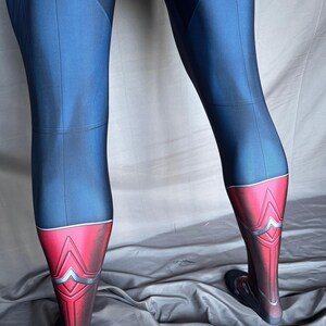 May include: Blue and red leggings with a geometric design on the lower legs. The leggings have a dark blue upper section and a red lower section with silver accents. The fabric appears to be a smooth, stretchy material.