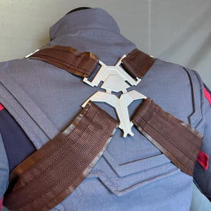 Puede incluir: Un disfraz gris y azul con correas marrones y una pieza de metal plateado en la espalda. Las correas son ajustables y se cruzan sobre los hombros.