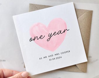 May include: A white card with a pink watercolour heart that says "one year" in black script. The card also says "As Mr and Mrs Cooper 01.09.2024" in black text.