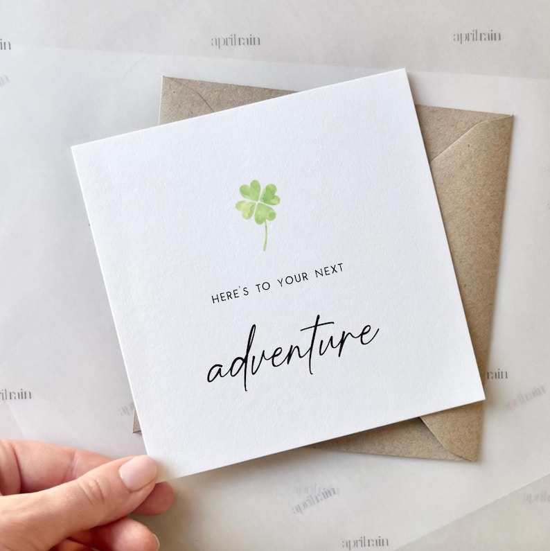 May include: A white card with a green four-leaf clover and the text "Here's to your next adventure".
