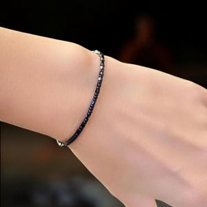 Op de afbeelding: Een delicate armband gemaakt van kleine zwarte en zilveren kralen. De armband wordt om de pols gedragen.