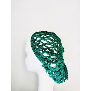 May include: A dark green crocheted hair net, displayed on a white mannequin head. The net features an open, lacy design. The hair accessory is a vibrant shade of green, and the background is plain white.