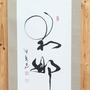 Peut inclure: Un rouleau de calligraphie japonaise traditionnel avec des coups de pinceau à l'encre noire sur papier blanc. L'œuvre comprend un grand cercle et des traits verticaux, avec des tampons rouges. Le rouleau est monté sur un fond vert clair.