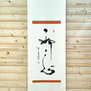 Peut inclure: Un rouleau vertical avec un design calligraphique. L'œuvre présente des coups de pinceau à l'encre noire sur papier blanc, avec des bandes décoratives rouges en haut et en bas. Le rouleau est suspendu par une chaîne métallique et possède une baguette en bois en bas.