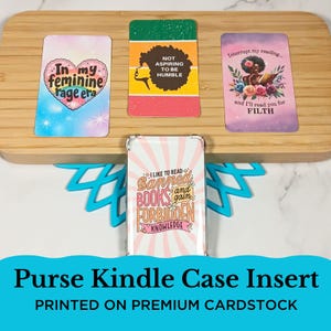 May include: A collection of purse Kindle case inserts with various designs. One features a heart with the text "In my feminine rage era." Another has the text "Not aspiring to be humble." A third says "Interrupt my reading... and I'll read you for filth."
