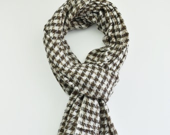 May include: A brown and white houndstooth patterned scarf. The scarf is folded and draped over a white surface.