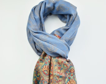 May include: A blue and beige patterned scarf with a fringed edge. The scarf features a paisley design and a striped pattern.