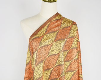 May include: A brown, orange, and gold patterned shawl with a paisley design. The shawl is draped over a white mannequin.
