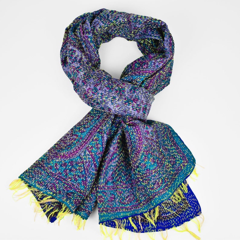 Puede incluir: Una bufanda de seda con estampado azul, morado y amarillo con flecos. La bufanda est&aacute; doblada en un bucle y tiene un dise&ntilde;o paisley.