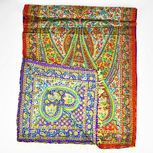 Puede incluir: Una colcha kantha de colores con estampado de paisley y borde rojo. La colcha est&aacute; doblada por la mitad y el estampado es visible en ambos lados.