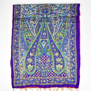 Puede incluir: Una bufanda de seda con estampado paisley morado y azul con borde rojo. La bufanda tiene un borde con flecos.