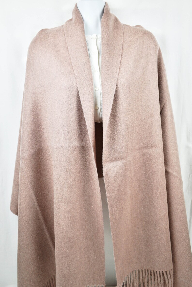 May include: A soft, light brown shawl with a fringed edge. The shawl is made of a fine, lightweight fabric and is perfect for adding a touch of warmth and style to any outfit.