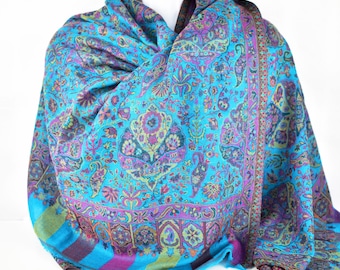 May include: A blue paisley patterned shawl with a purple, green and gold border. The shawl is folded and draped over a white mannequin.