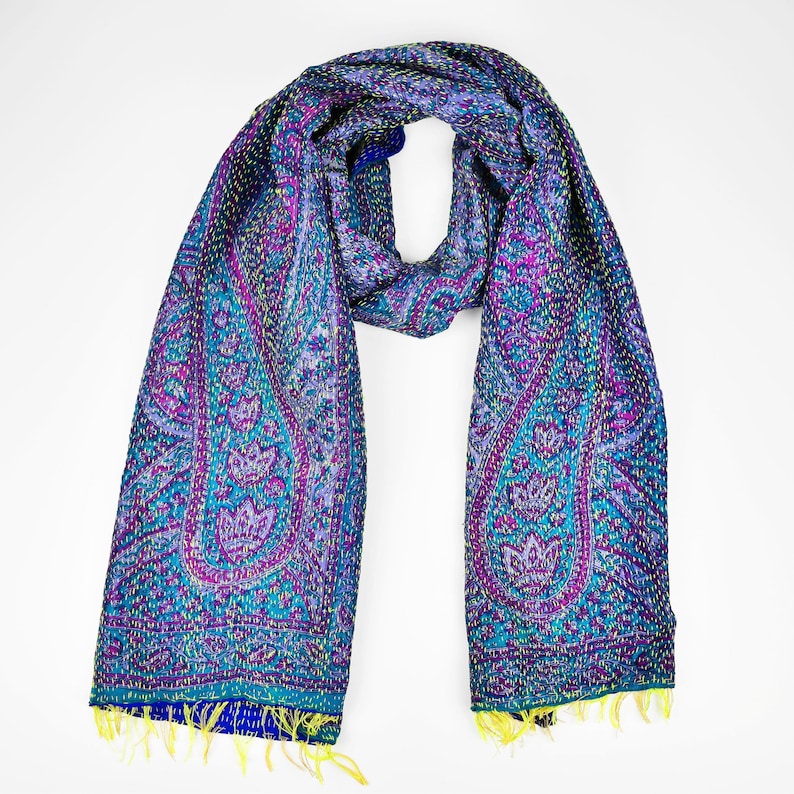 Puede incluir: Una bufanda de seda azul y morada con estampado de paisley, costuras amarillas y flecos azules.