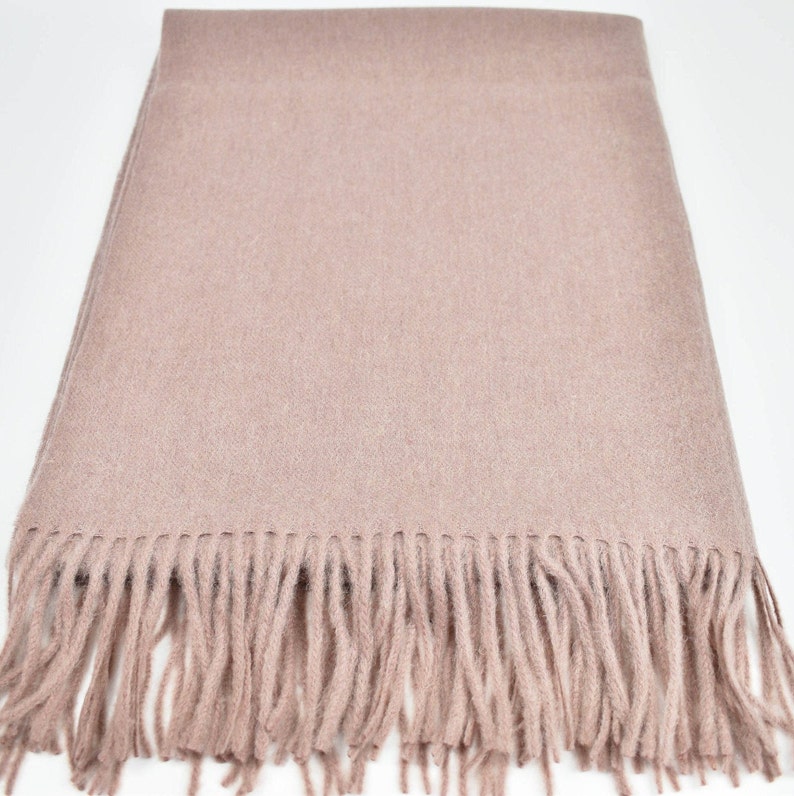 May include: A soft, light pink scarf with a fringe border. The scarf is made of a fine, woven fabric.