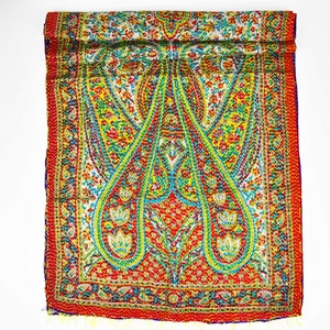 Puede incluir: Una bufanda de seda con estampado paisley de colores sobre fondo rojo con detalles en verde, amarillo y azul. La bufanda est&aacute; doblada por la mitad y tiene un borde con flecos.