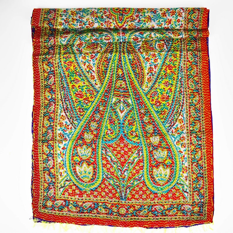 Puede incluir: Una bufanda de seda con estampado paisley de colores sobre fondo rojo con detalles en verde, amarillo y azul. La bufanda est&aacute; doblada por la mitad y tiene un borde con flecos.