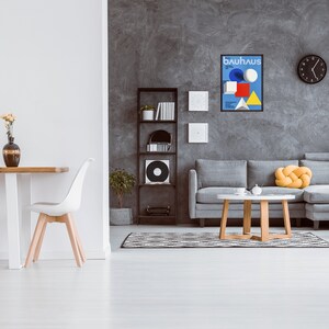 May include: A living room interior with a gray sofa, a wooden coffee table, and a black and white rug. A black framed poster with the text "bauhaus" is hanging on the wall. There is a bookshelf with books and a record player in the background.