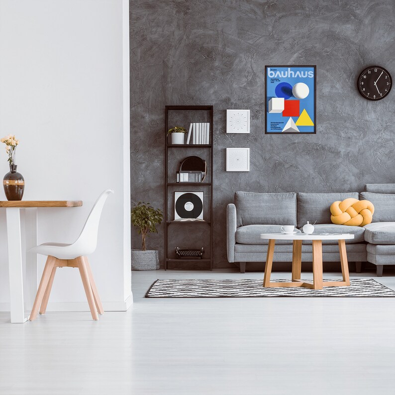 May include: A living room interior with a gray sofa, a wooden coffee table, and a black and white rug. A black framed poster with the text "bauhaus" is hanging on the wall. There is a bookshelf with books and a record player in the background.