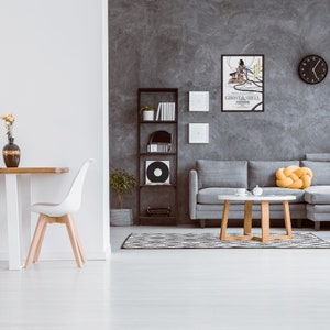 May include: A living room interior with a gray sectional sofa, a coffee table, a black bookshelf, a white dining chair, and a framed movie poster for "Ghost in the Shell" on a gray wall.