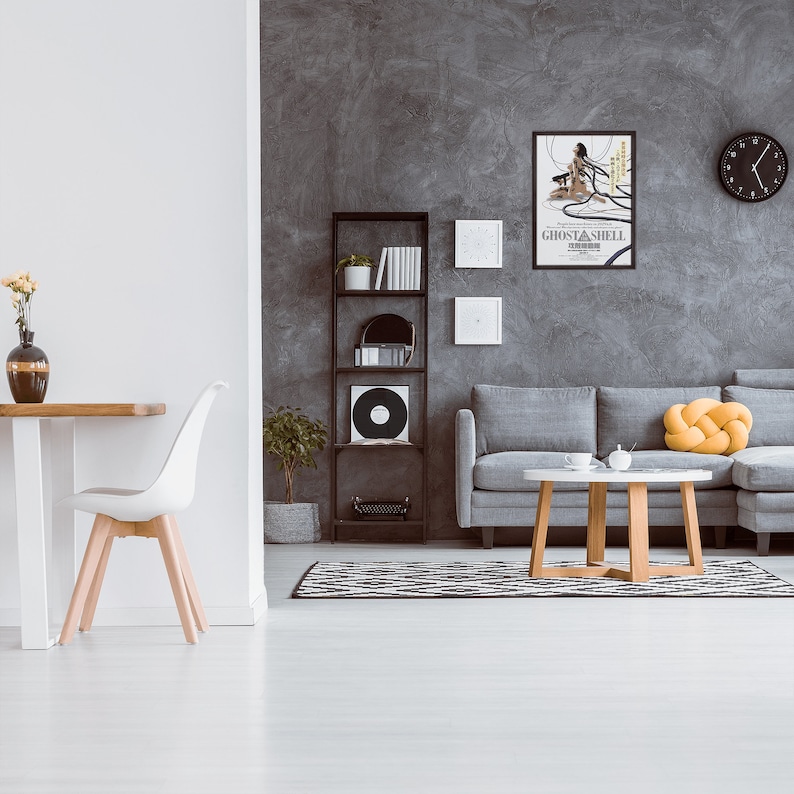 May include: A living room interior with a gray sectional sofa, a coffee table, a black bookshelf, a white dining chair, and a framed movie poster for "Ghost in the Shell" on a gray wall.