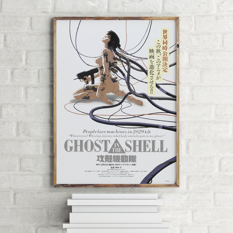 May include: A poster for the anime film "Ghost in the Shell" featuring a woman with a cybernetic body and wires connected to her. The text on the poster reads "People love machines in 2029 A.D." and "Ghost in the Shell".