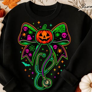 May include: Black sweatshirt with a Halloween design. The graphic features a neon-coloured jack-o'-lantern, bow, stethoscope, spiders, skulls, and stars. The design is centered on the front of the sweatshirt.