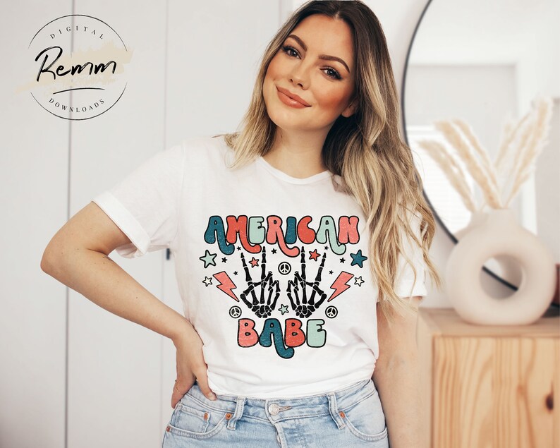 May include: White t-shirt with a colorful graphic design that says "American Babe" with peace signs, lightning bolts, and stars.