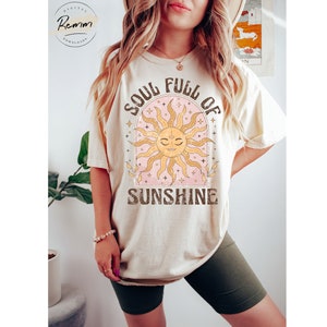 Puede incluir: Una camiseta beige con un gr&aacute;fico de un sol con cara y el texto "Soul Full of Sunshine".