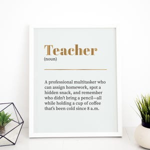 Puede incluir: Una impresión enmarcada en blanco con la palabra "Teacher" en letras doradas y una definición de un maestro. La definición dice: "Un multitarea profesional que puede asignar tareas, detectar un refrigerio oculto y recordar quién no trajo un lápiz, todo mientras sostiene una taza de café que ha estado fría desde las 8 a.m."