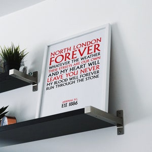 May include: White framed print with red text that reads "North London Forever" and "Whatever the weather these streets are our own and my heart will leave you never my blood will forever run through the stone." The bottom of the print reads "Arsenal F.C. Est 1886".