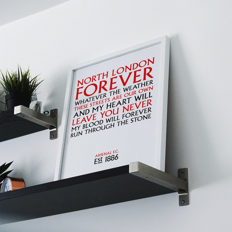 May include: White framed print with red text that reads "North London Forever" and "Whatever the weather these streets are our own and my heart will leave you never my blood will forever run through the stone." The bottom of the print reads "Arsenal F.C. Est 1886".