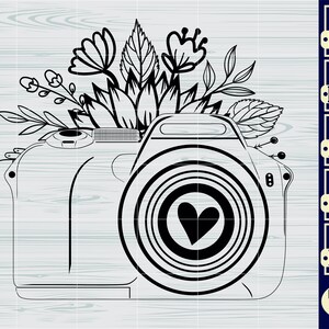 May include: Black and white line art illustration of a camera with a heart in the lens. The camera is surrounded by flowers and leaves.