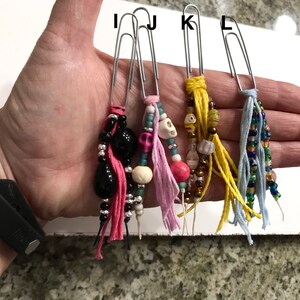 May include: Four silver paper clips with colorful beaded and tassel charms. The charms include pink, blue, yellow, and black tassels with beads in various colors and shapes.