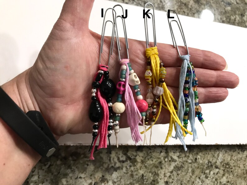 May include: Four silver paper clips with colorful beaded and tassel charms. The charms include pink, blue, yellow, and black tassels with beads in various colors and shapes.