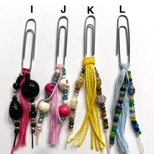 May include: Four silver paper clips with colorful beaded and tassel charms. The charms include black, white, pink, blue, yellow, and brown beads. The tassels are pink, blue, yellow, and white.