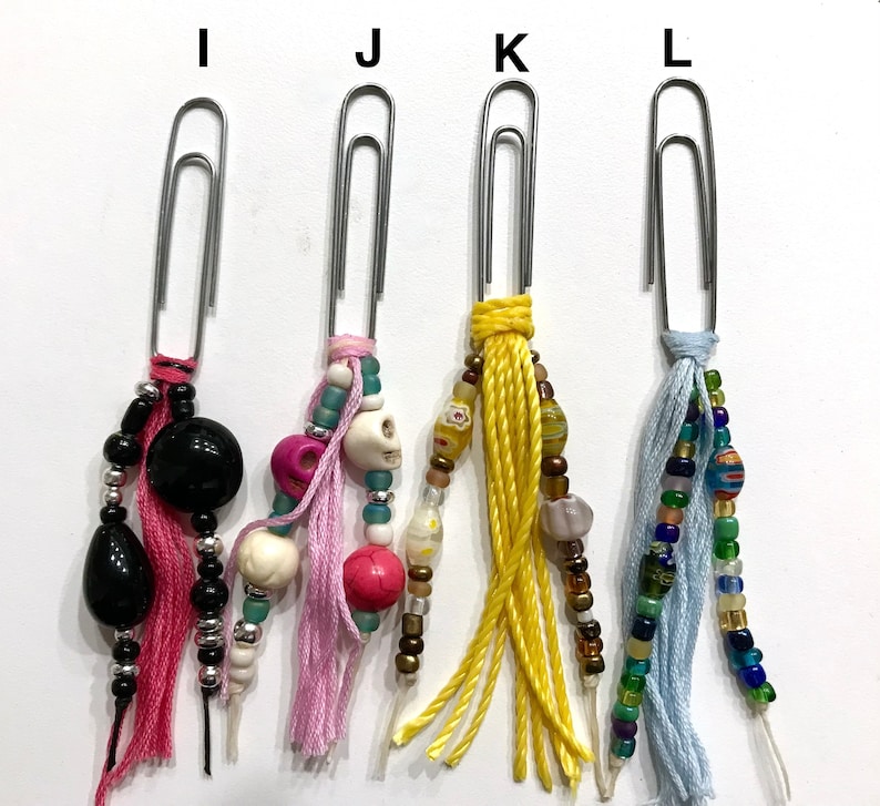 May include: Four silver paper clips with colorful beaded and tassel charms. The charms include black, white, pink, blue, yellow, and brown beads. The tassels are pink, blue, yellow, and white.