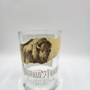 May include: A clear glass tumbler with a torn label showing a sepia-toned bison image. The label also includes the text "BUFFALO TRACE" and "KENTUCKY STRAIGHT BOURBON WHISKEY".