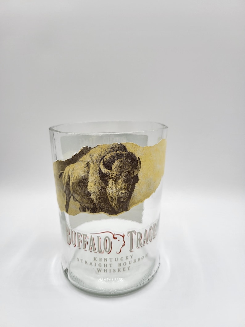 May include: A clear glass tumbler with a torn label showing a sepia-toned bison image. The label also includes the text "BUFFALO TRACE" and "KENTUCKY STRAIGHT BOURBON WHISKEY".