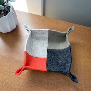 May include: A small, square-shaped felt tray with four sections. The sections are in shades of gray, red, and black. The tray is perfect for organizing small items on a desk or nightstand.