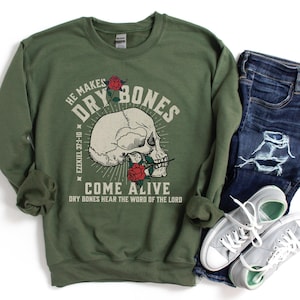 May include: A green sweatshirt with a skull and roses graphic. The text on the sweatshirt reads "He Makes Dry Bones Come Alive" and "Ezekiel 37:1-10" and "Dry Bones Hear The Word Of The Lord".