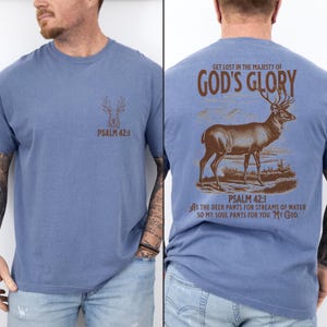 A blue t-shirt with a brown deer silhouette and the text 'PSALM 42:1' on the front. The back has a larger brown deer silhouette and the text 'GET LOST IN THE MAJESTY OF GOD'S GLORY'. Mens Christian Shirts, Bible Verse Shirt, Hunting Gifts, Husband Gift, Deer Hunter, Father's Day Gift, Jesus Shirt, Adult Baptism Gifts, Men's Shirt, Religious Shirt, Christian Gift, Religious Gift For Men, Hunting T-shirt, Deer Tshirt, Comfort Colors Tshirt