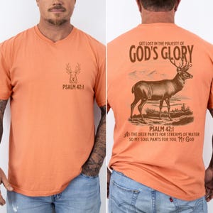 A bright orange t-shirt with a brown deer silhouette and the text 'PSALM 42:1' on the front. The back of the shirt has a brown deer illustration with the text 'GET LOST IN THE MAJESTY OF GOD'S GLORY'. Mens Christian Shirts, Bible Verse Shirt, Hunting Gifts, Husband Gift, Deer Hunter, Father's Day Gift, Jesus Shirt, Adult Baptism Gifts, Men's Shirt, Religious Shirt, Christian Gift, Religious Gift For Men, Hunting T-shirt, Deer Tshirt, Comfort Colors Tshirt